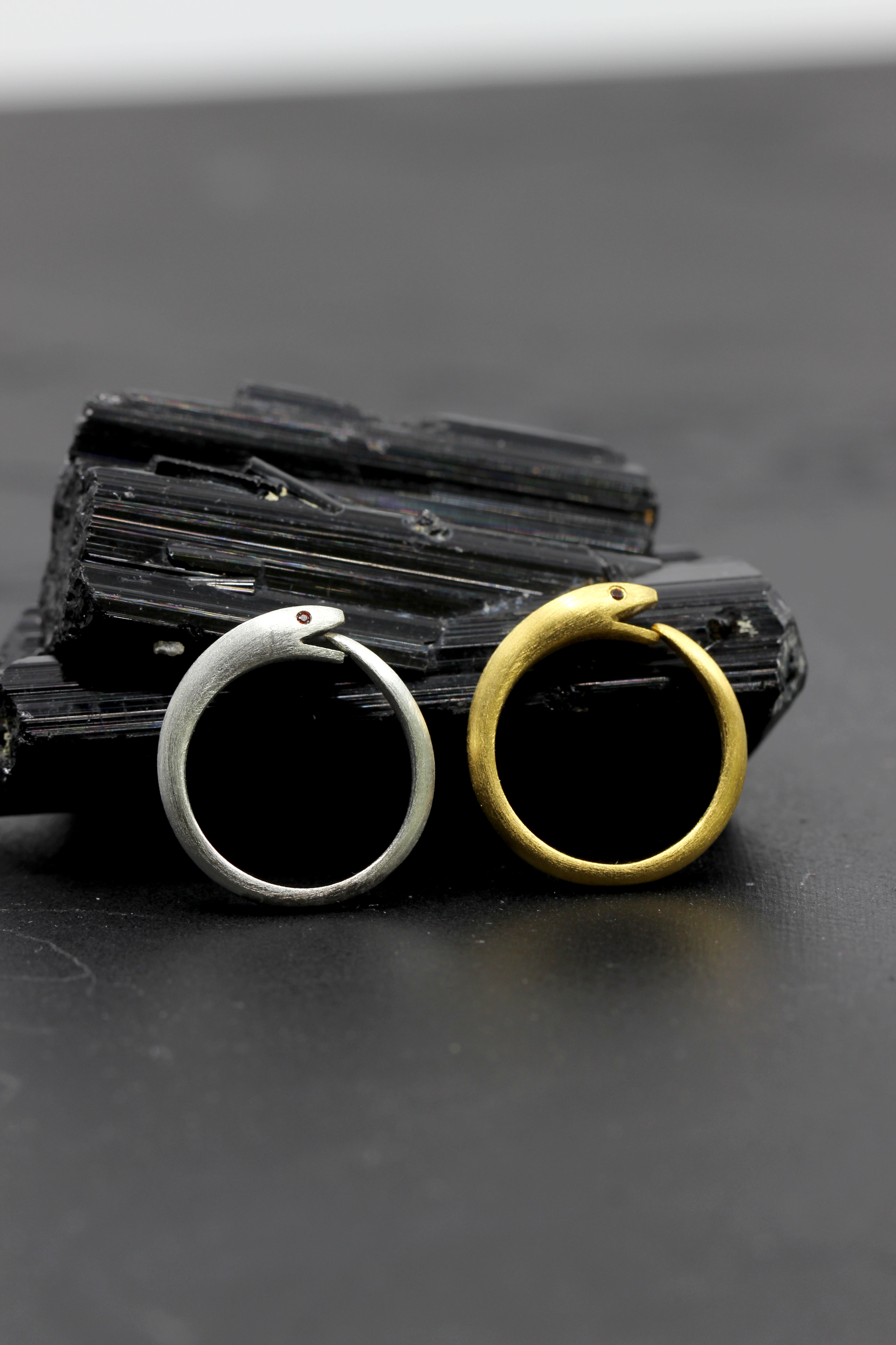 Photo of gold and silver finishes of Ouroboros snake ring with ruby-red CZ eyes, symbolizing transformation from Blackbird Designs.